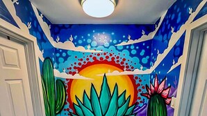 A narrow hallway with a vibrant mural featuring a desert landscape, cacti, and a sunset.