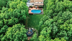 A house surrounded by dense green trees, with a swimming pool and outdoor seating area. - Pocono Escape with huge Pool HOT TUB,GAMEROOM,FIREPIT,near Camelback & Kalahari (Stroudsburg)