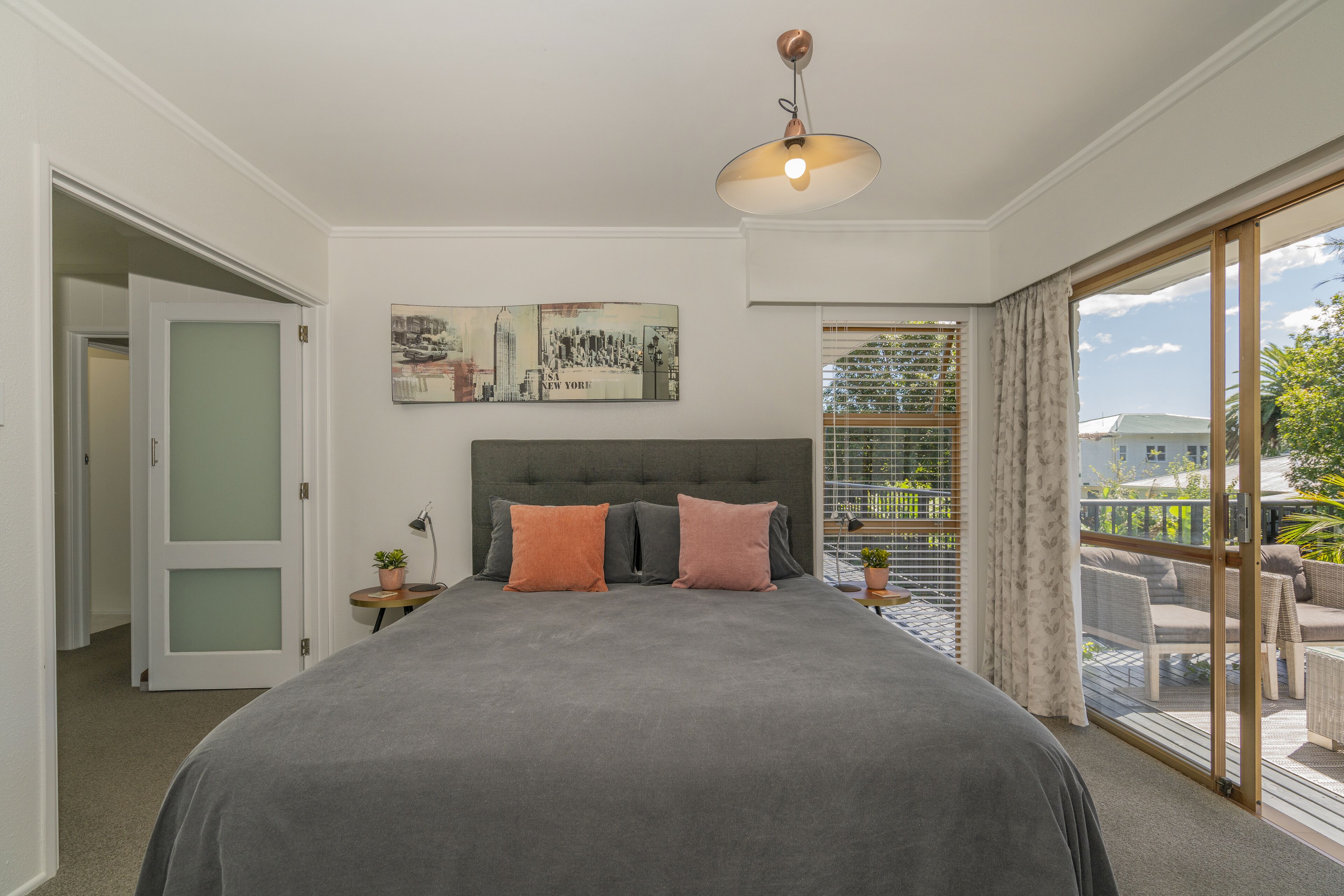 A bedroom with a large bed, a ceiling light, a window with curtains, and a view of the outside.