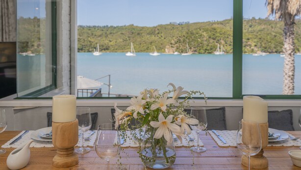 A dining table set with candles, a vase of flowers, and a view of a lake with sailboats. - Oceans 88 Whitianga Coastal Accommodation Suites (Whitianga)