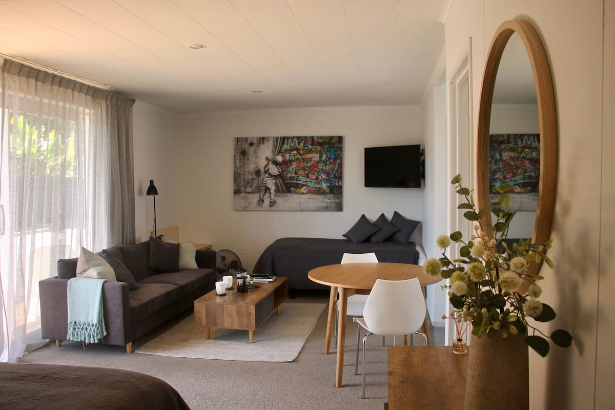 Una sala de estar moderna con un sofá, una mesa de centro, una mesa de comedor con sillas, un espejo grande y un cuadro en la pared.