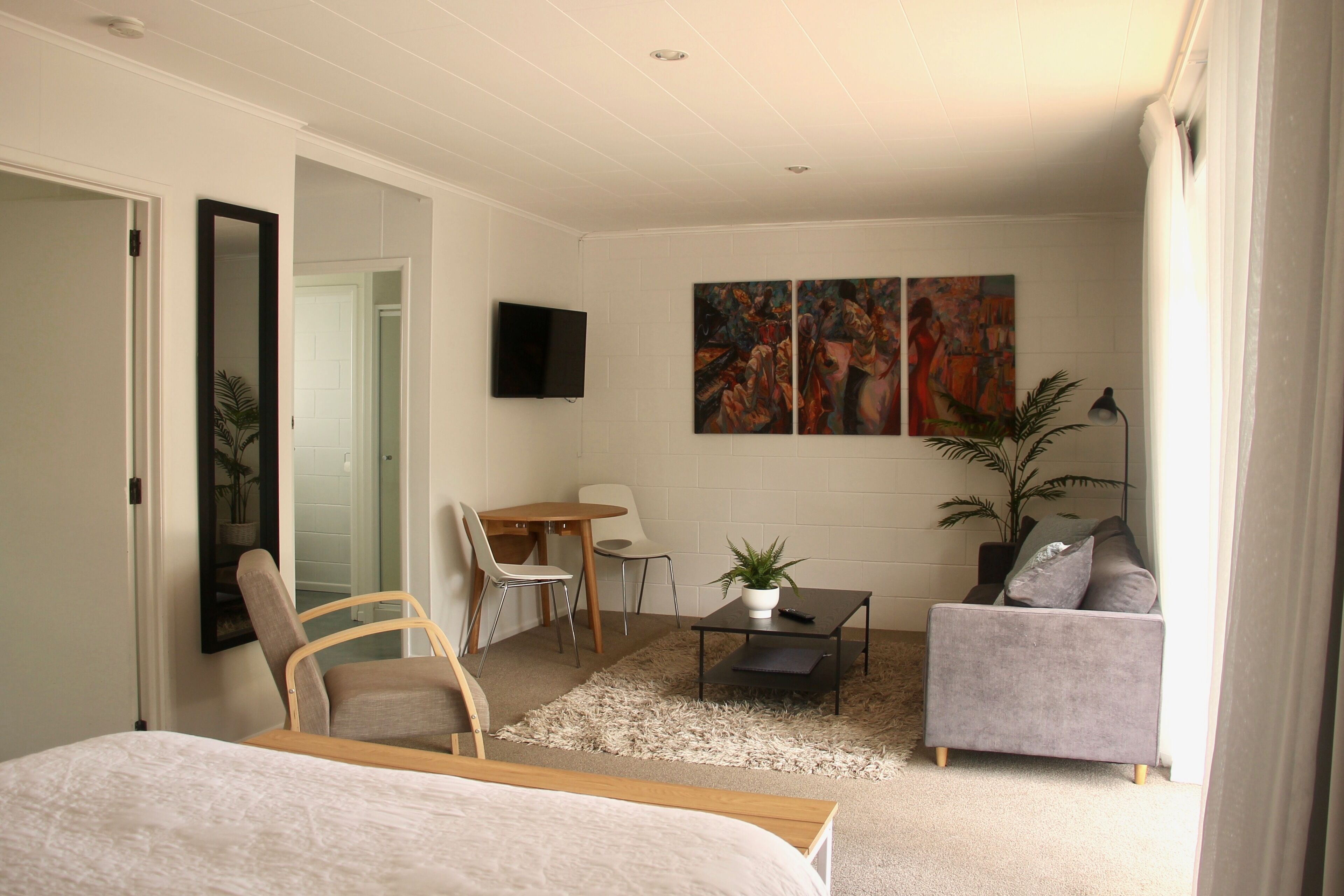A modern hotel room with a bed, a desk, a sofa, and two paintings on the wall.