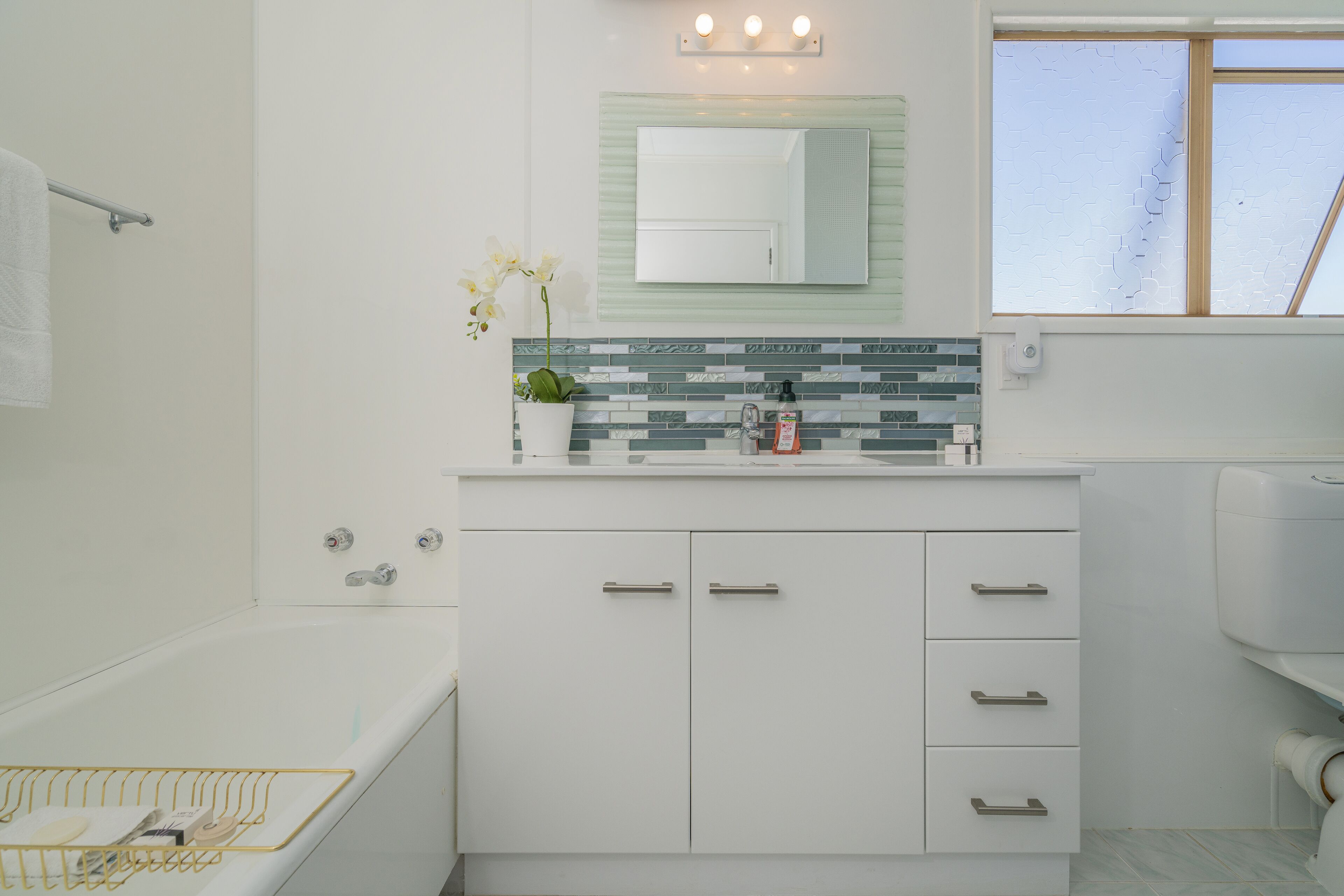 Une salle de bain moderne avec une baignoire blanche, un meuble-lavabo avec un pare-éclaboussures carrelé et un miroir au-dessus du lavabo.