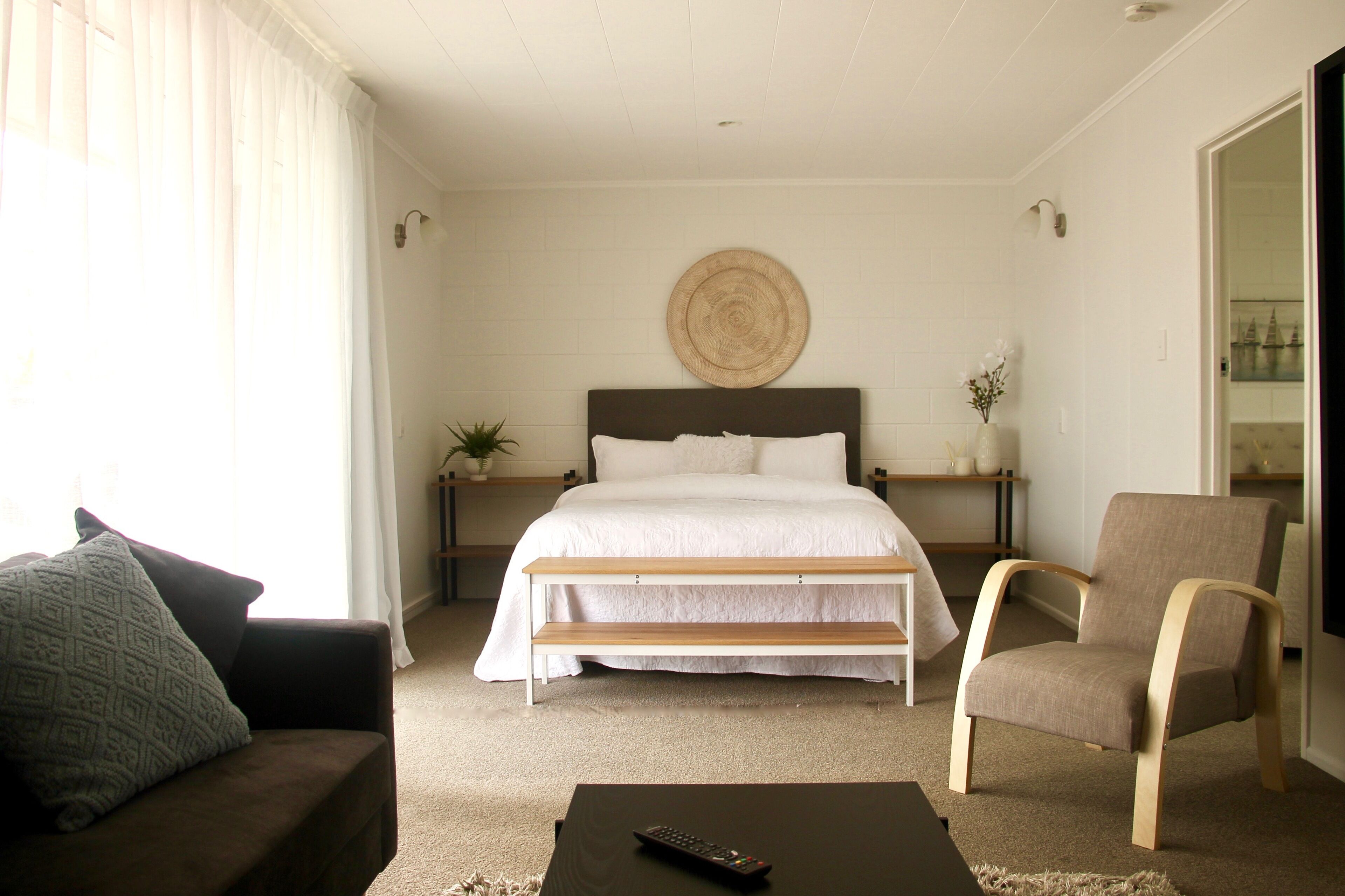 A bedroom with a bed, a bedside table with a plant, a chair, and a couch.