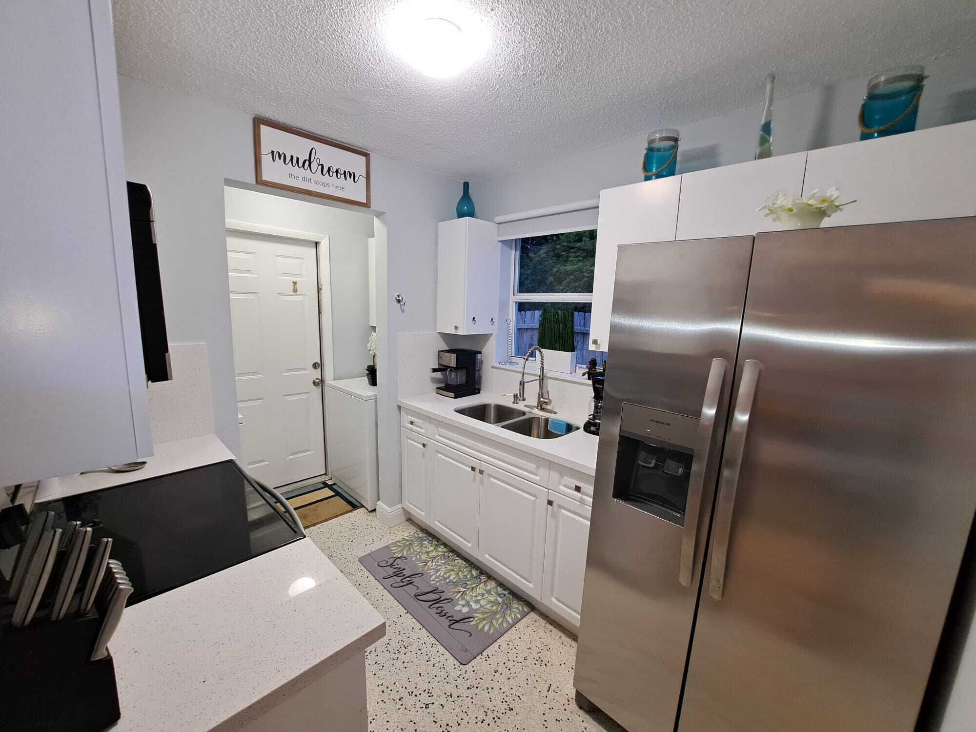 A compact kitchen with white cabinets, a stainless steel refrigerator, a coffee maker, and a window with a view of greenery.