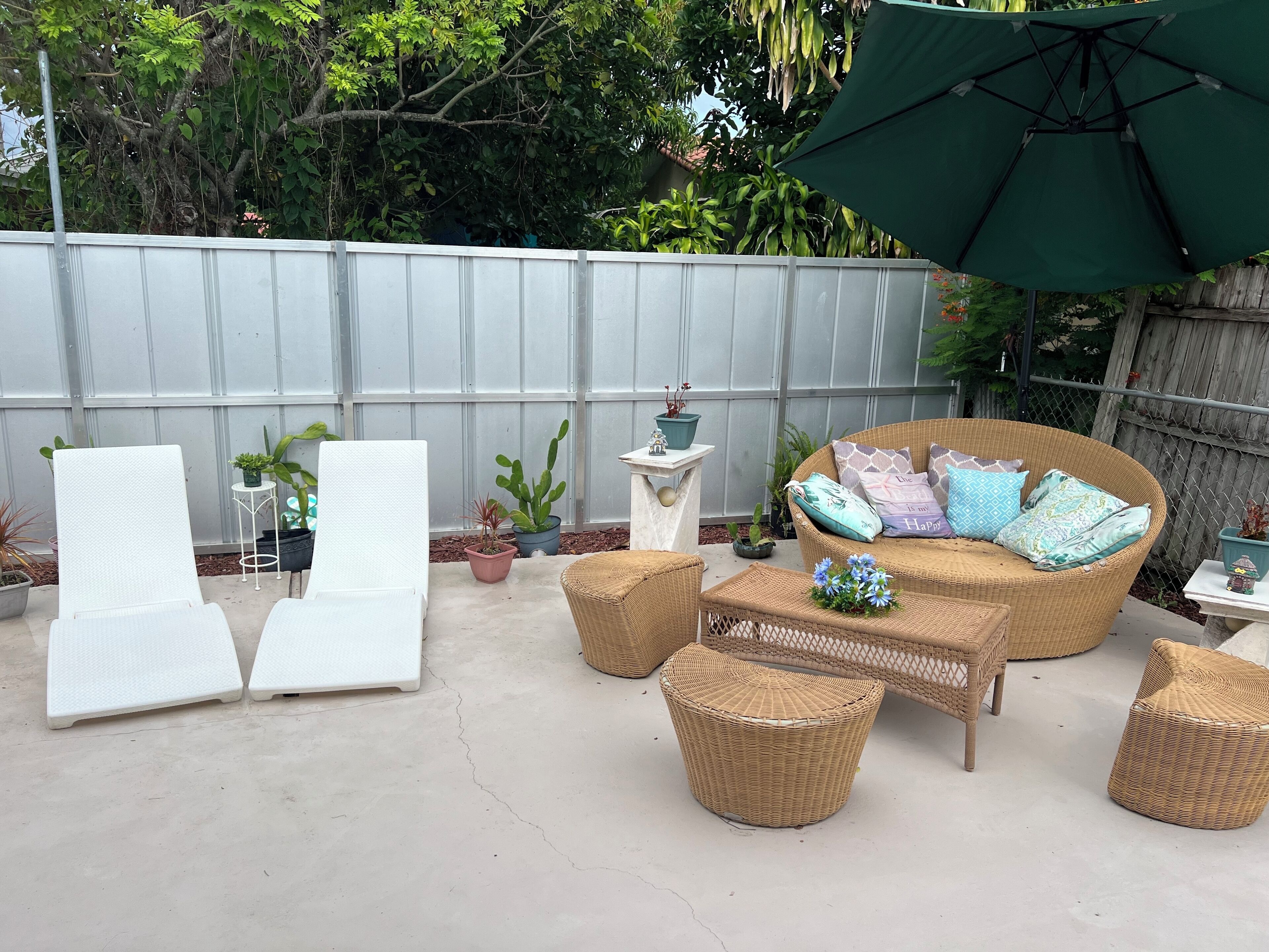 Een terras buiten met rieten meubels, plantenbakken en een groene parasol.