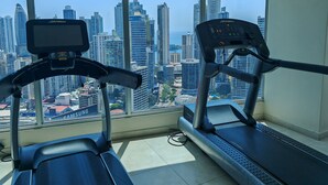 A gym with two treadmills and a large window offering a city view. - Beutiful High Floor Apartment in the Best Location (Panamá)