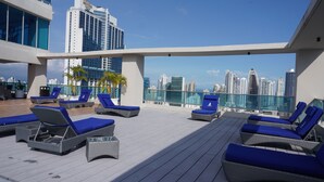 A rooftop lounge with blue cushioned chairs and a glass balustrade overlooking a cityscape. - Beutiful High Floor Apartment in the Best Location (Panamá)