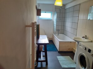 Une salle de bain compacte comprenant une baignoire, un lavabo et un lave-linge.