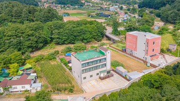 Vista aérea de una zona residencial con un edificio moderno de dos pisos, una estructura con techo verde y vegetación circundante.
