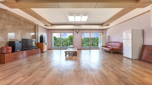 Un salón amplio con suelo de madera, televisor, sofá y refrigerador.