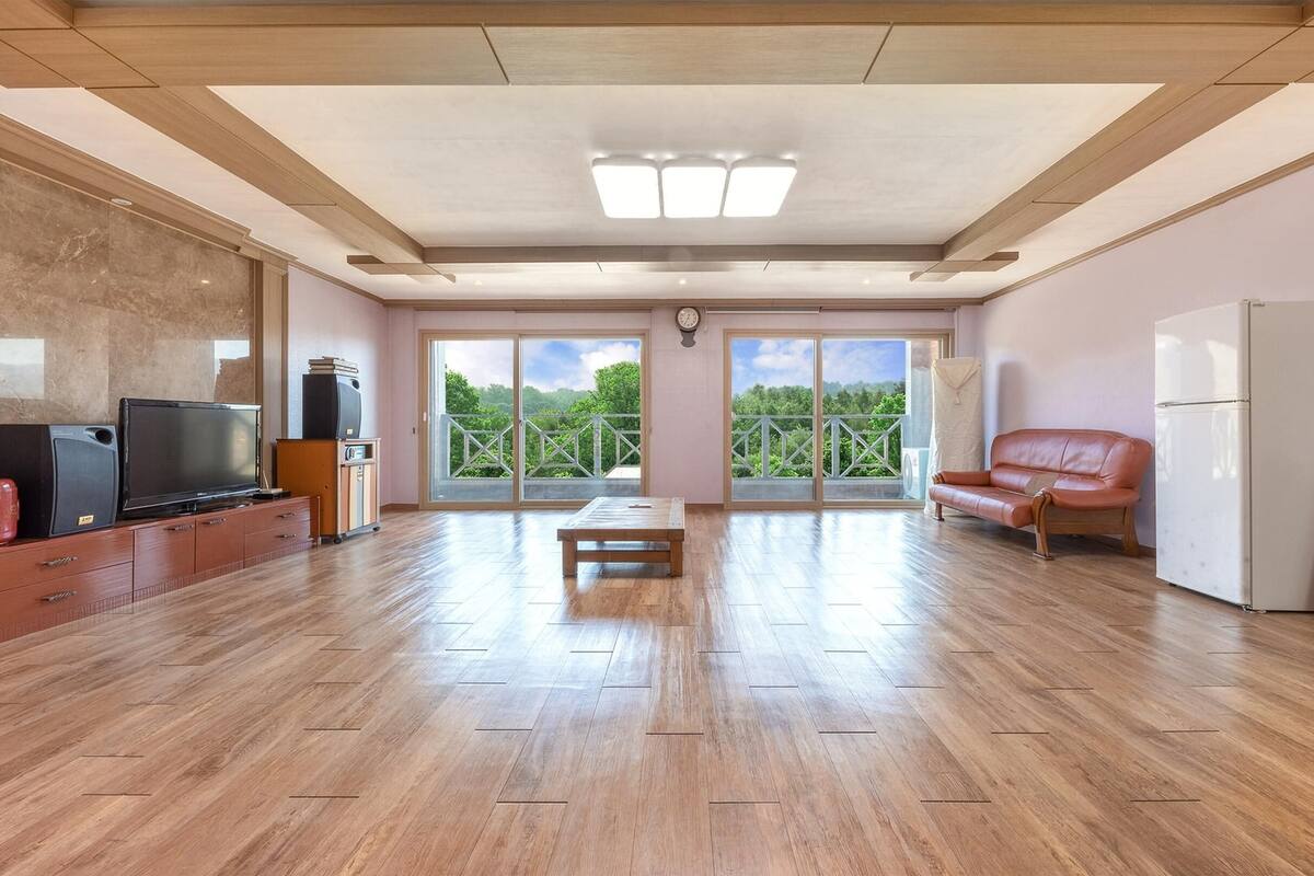 Un salón amplio con suelo de madera, televisor, sofá y refrigerador.