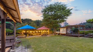 Un patio trasero con un área de terraza techada, mesas de picnic y un árbol grande.