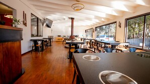 Interno di un ristorante moderno con pavimenti in legno, tavoli neri e un'ampia finestra che offre vista sull'esterno.
