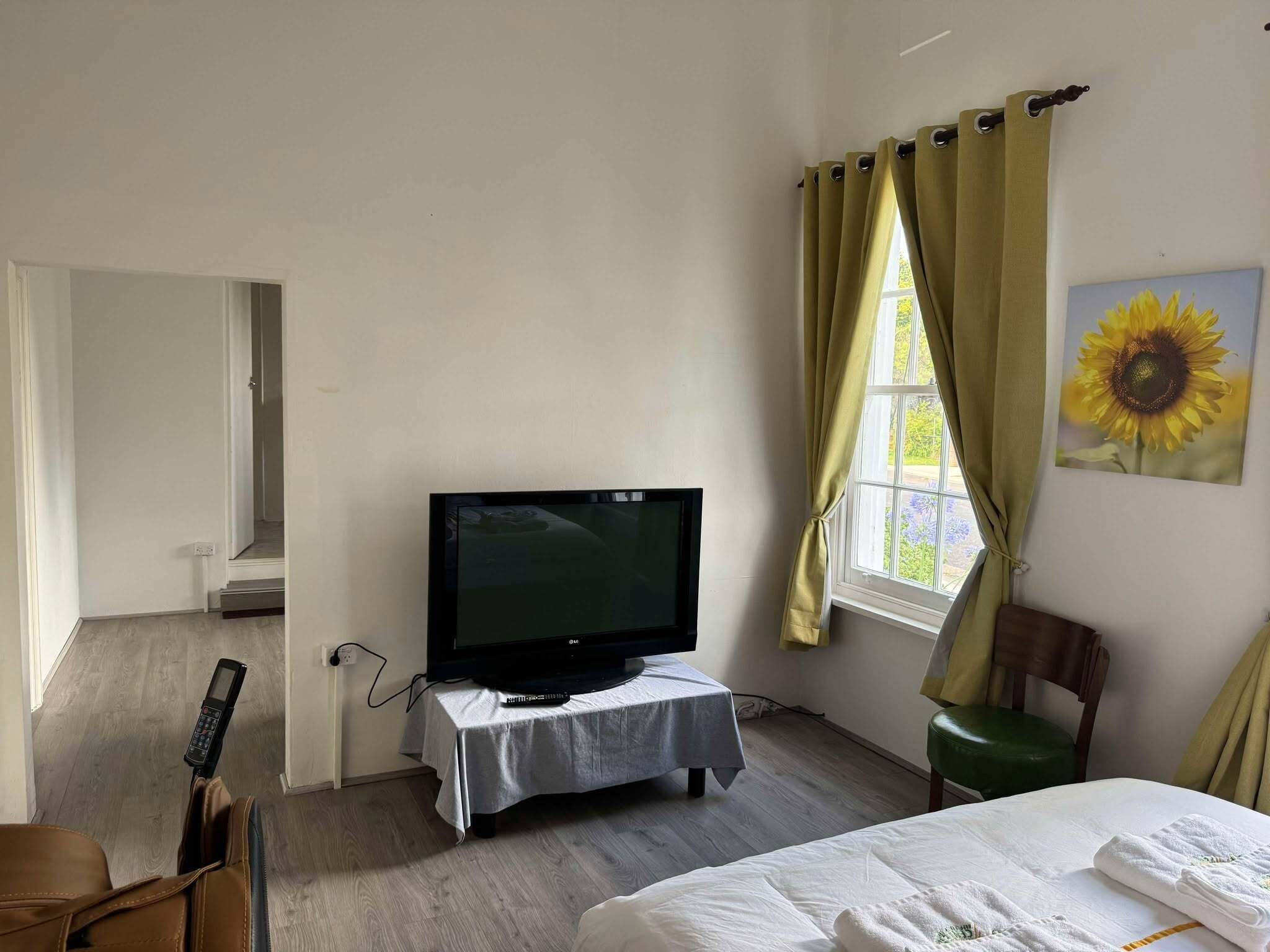 A hotel room with a television on a small table, a bed with white linens, a green chair, and a window with curtains.
