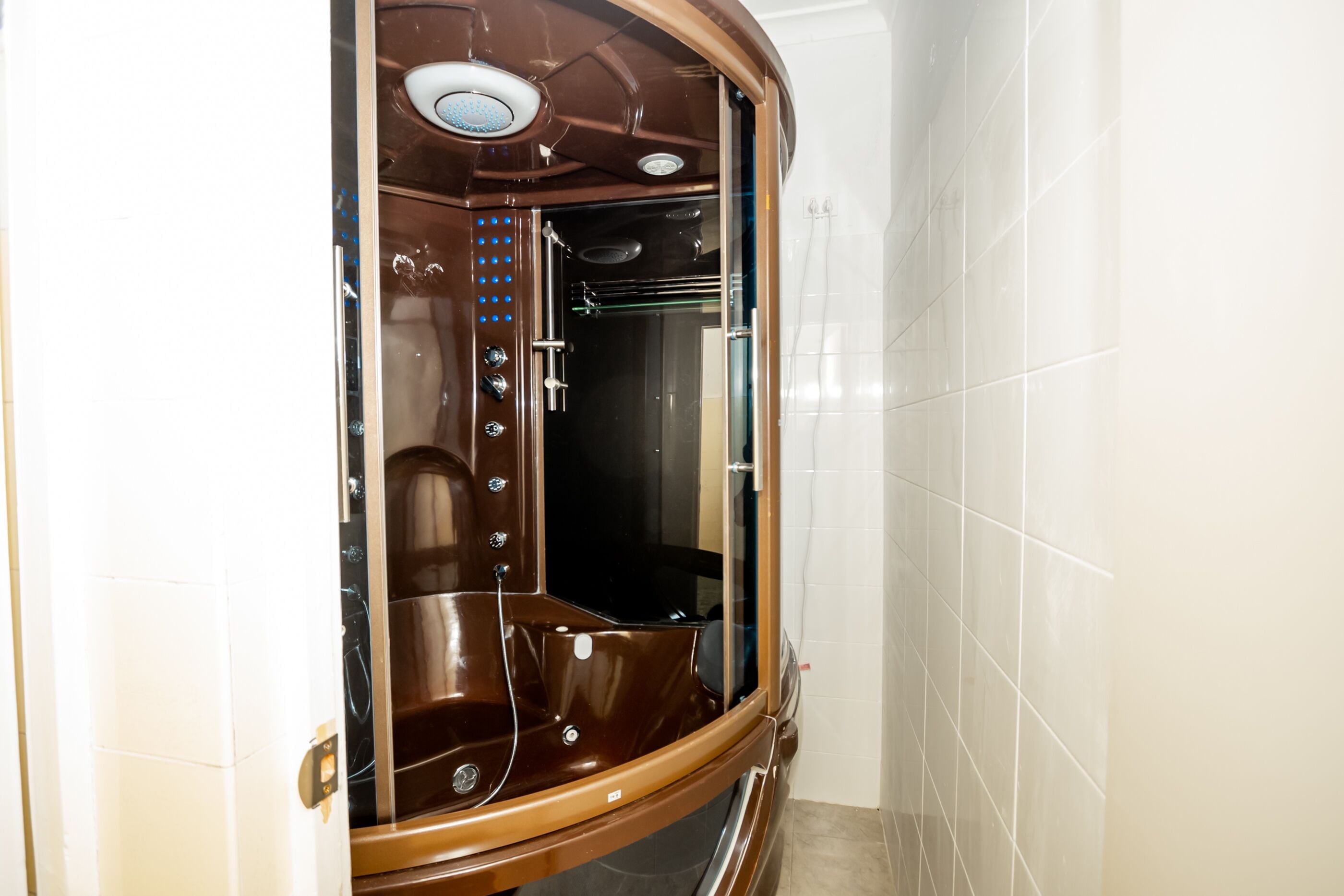 A modern bathroom with a glass-enclosed shower area, a visible control panel, and a tiled wall.