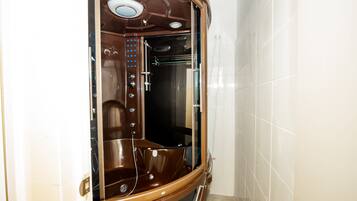 A modern bathroom with a glass-enclosed shower area, a visible control panel, and a tiled wall.