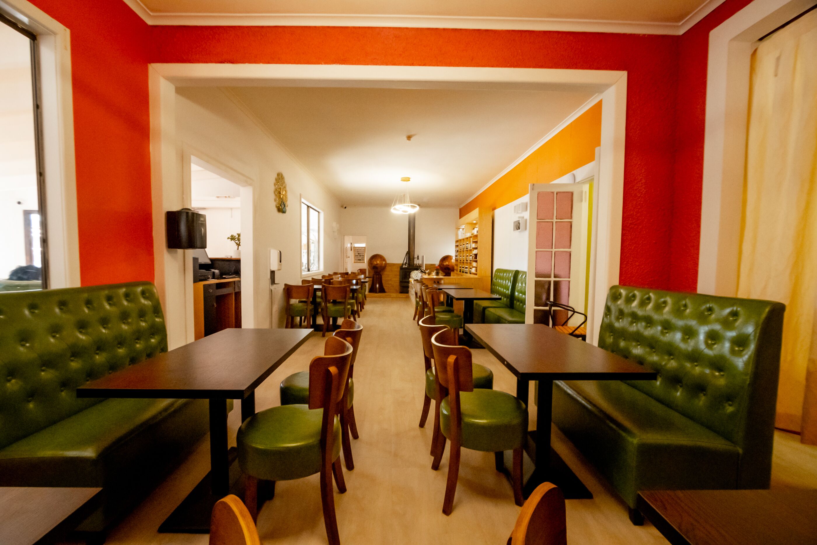 Un restaurant amb seients de color verd, taules de fusta, un passadís central i vista cap a la cuina.