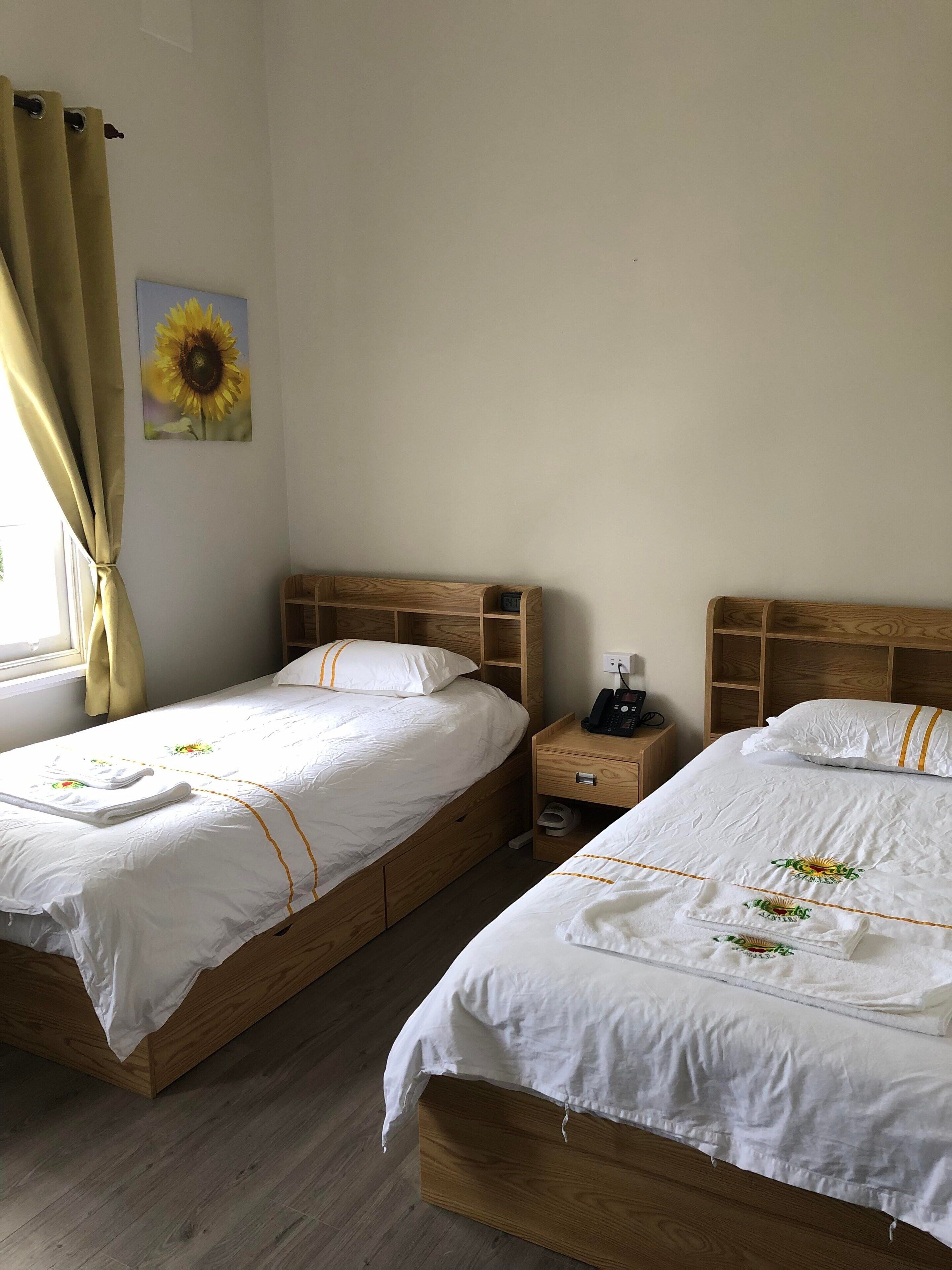 A hotel room with two wooden beds, each with white bedding and a small bedside table.