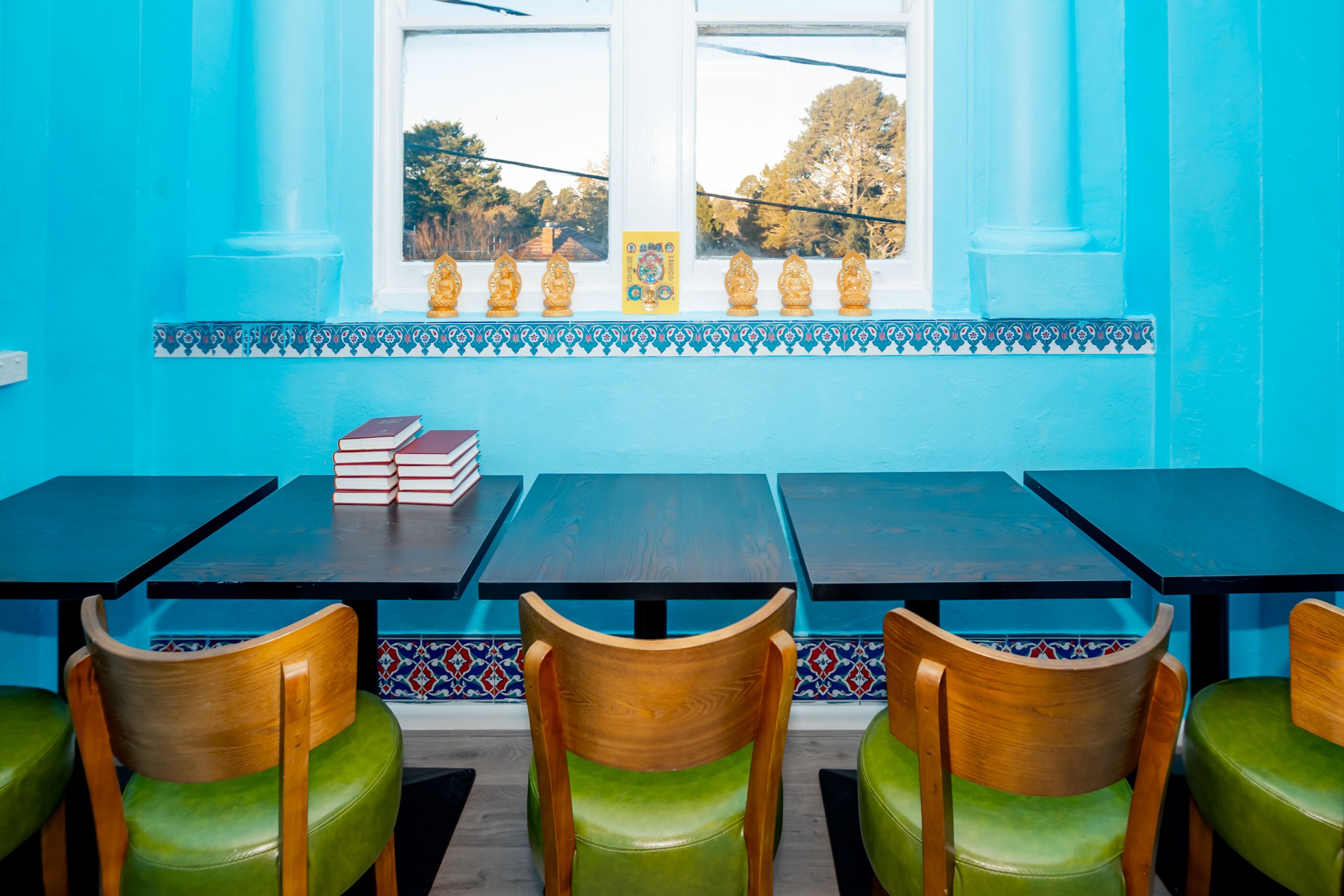 Una habitación con pared azul, una ventana decorada, un borde de azulejos y una mesa con sillas.