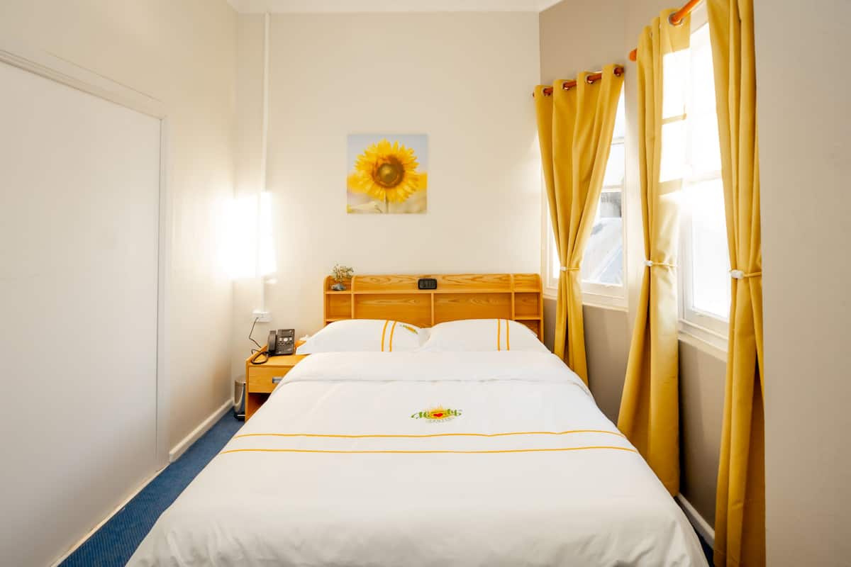 A hotel room with a bed, a nightstand, a lamp, a painting of a sunflower, and curtains.