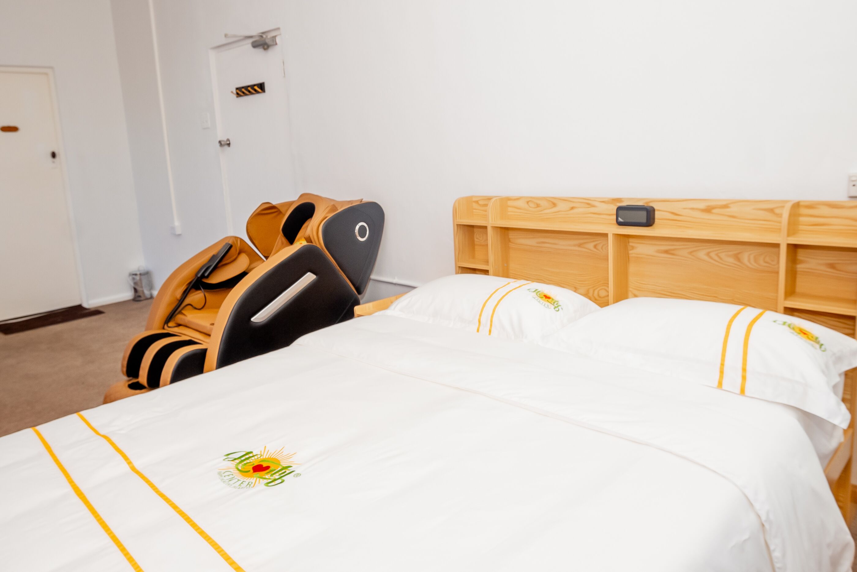 A hotel room with a wooden headboard, a bed with white bedding and yellow accents, a wooden bench, and a small table with a phone.