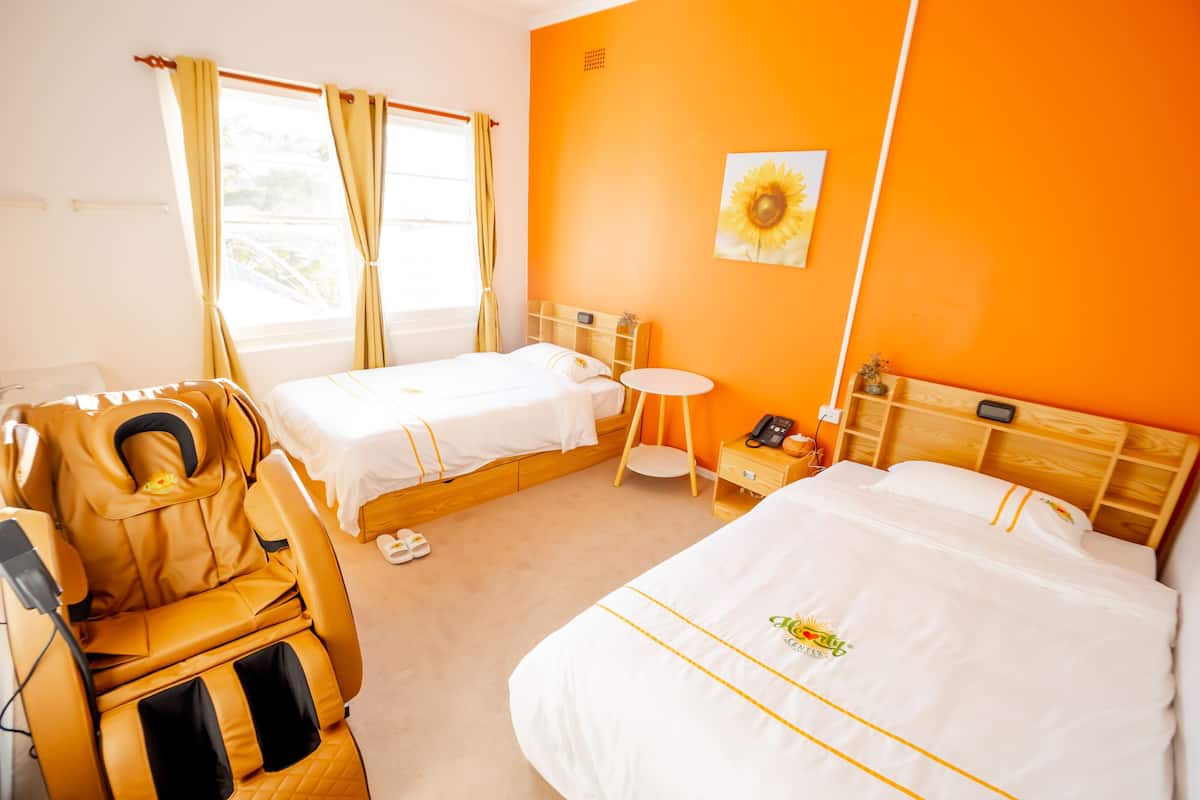 A hotel room with two beds, a massage chair, a small round table, and a wall-mounted phone.