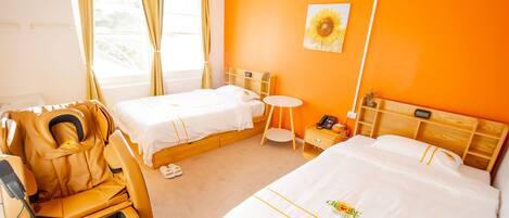 A hotel room with two beds, a massage chair, a small round table, and a wall-mounted phone.