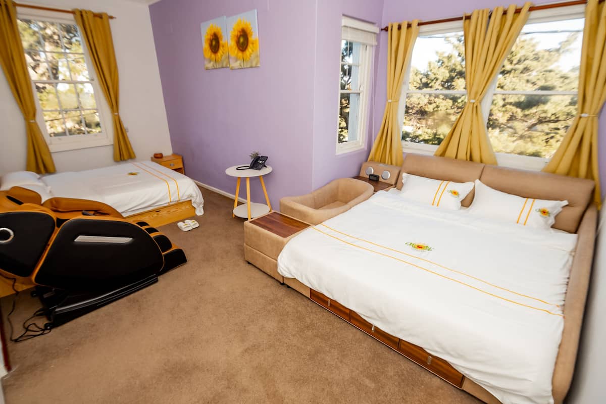 A bedroom with two beds, a massage chair, a small table, and a window with curtains.