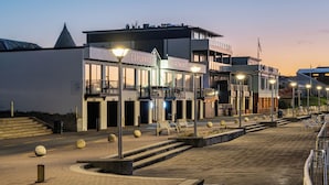 A modern building with "ESPLANADE" and "APARTMENTS" signage, featuring a balcony, outdoor seating, and a waterfront view. - Esplanade Apartments (Dunedin)