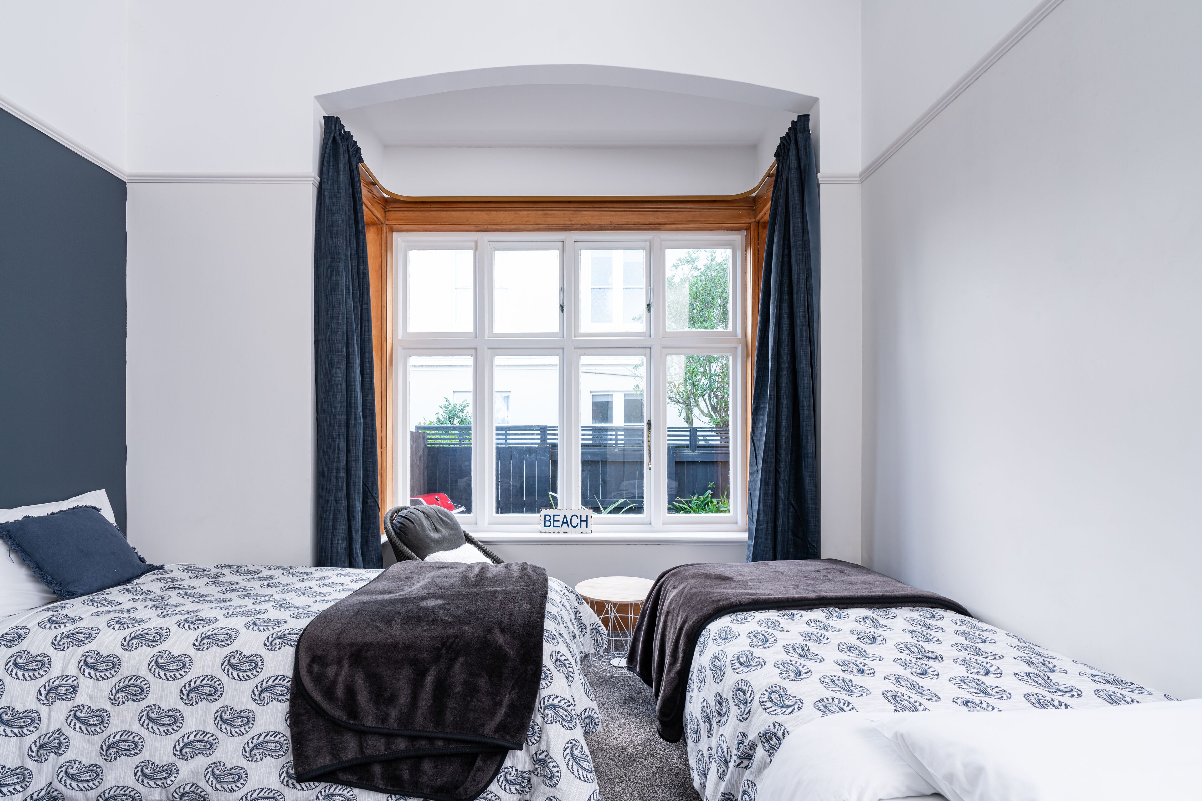 Habitación de hotel con dos camas, una mesita redonda y un ventanal con cortinas.