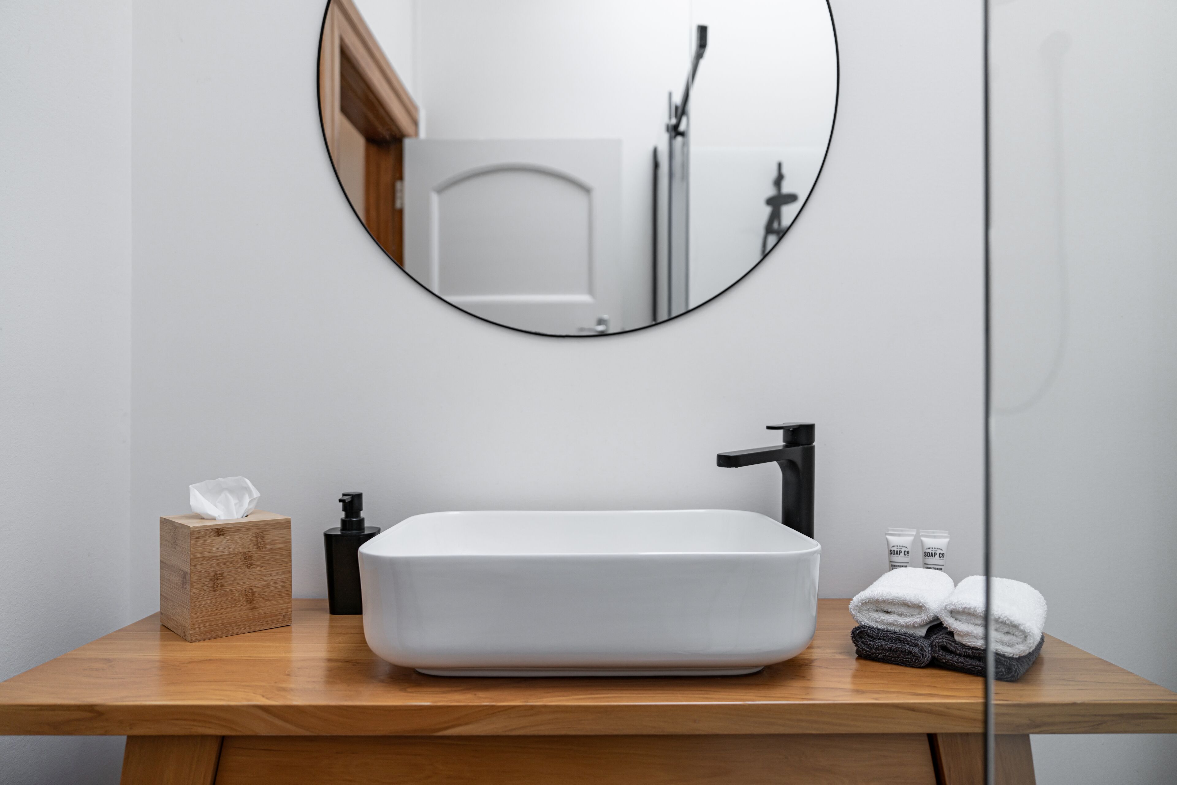 A bathroom with a white sink, a round mirror, and a wooden vanity.