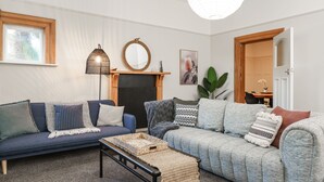 A living room with a blue sofa, a grey sofa, a coffee table, a fireplace, a mirror, and a hanging light fixture. - Esplanade Apartments (Dunedin)