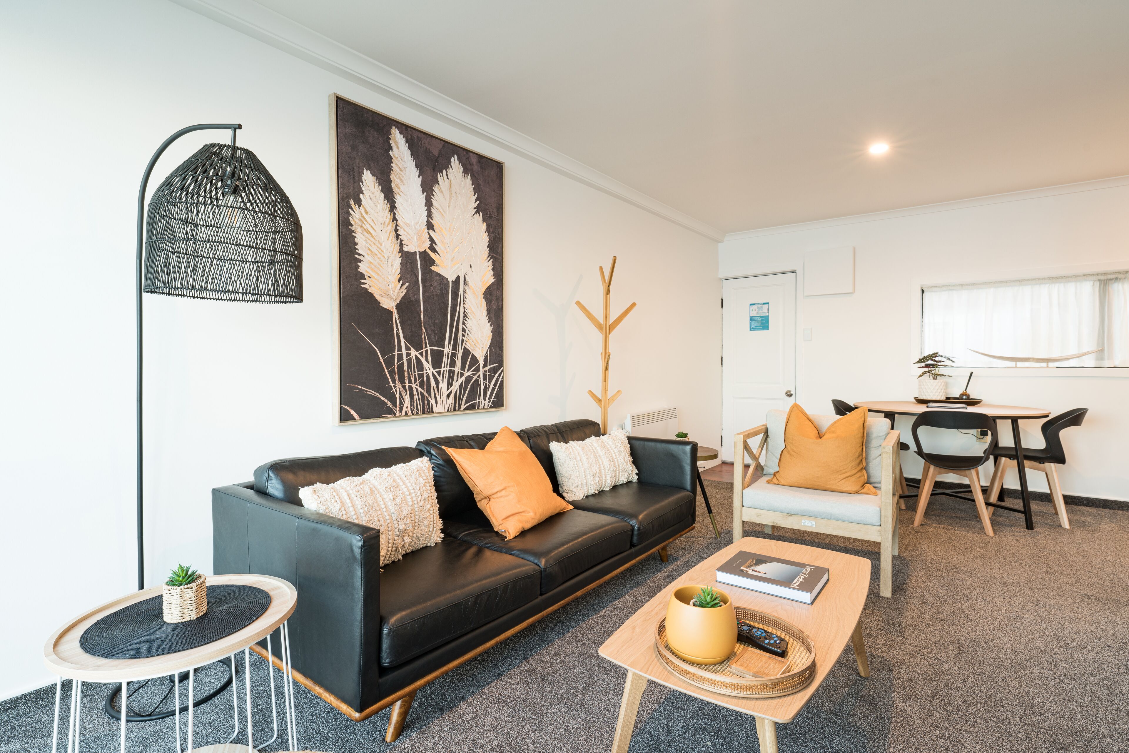 A modern living room with a black leather sofa, a wooden coffee table, and a dining area with a table and chairs.