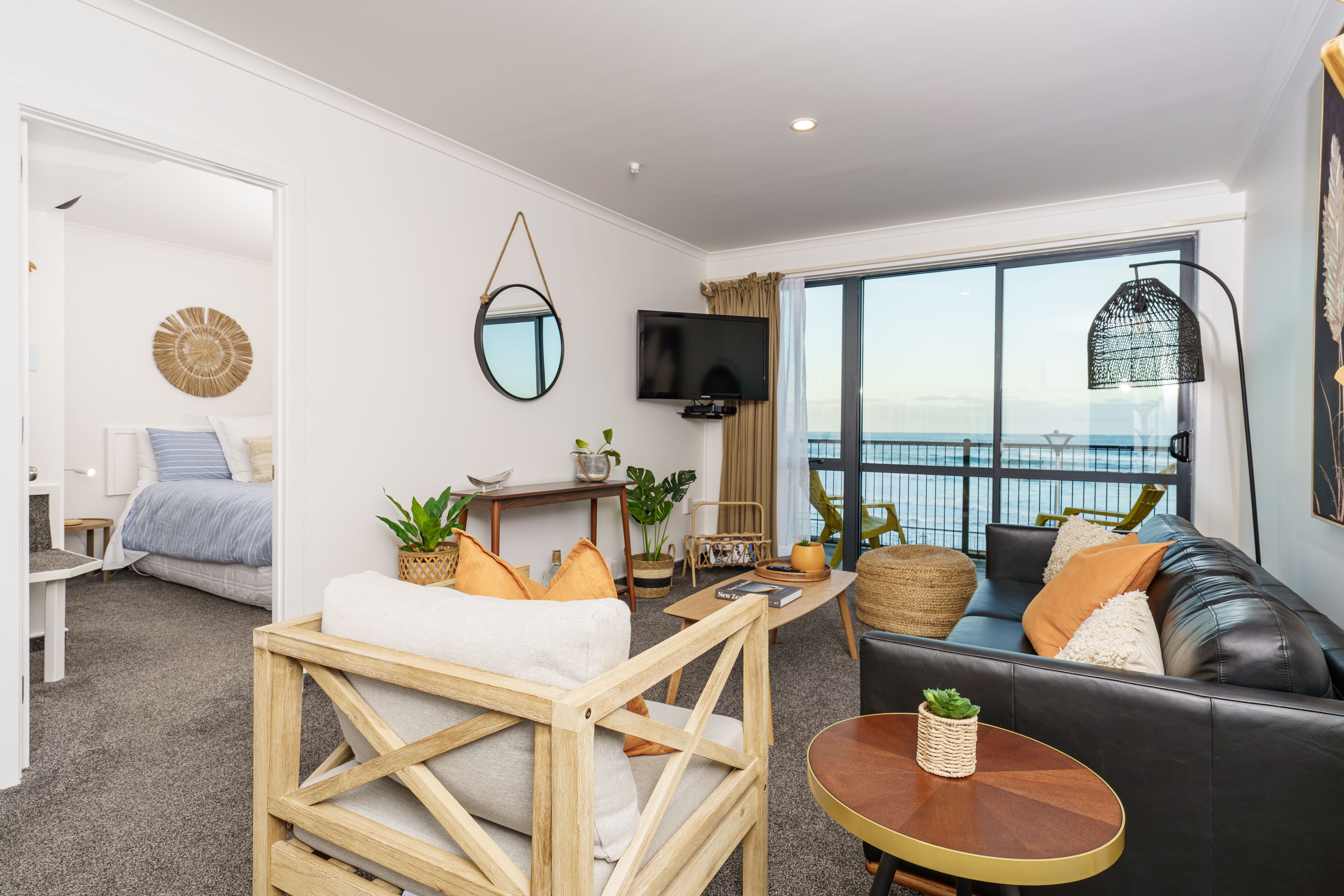 A modern living room with a sofa, a coffee table, a TV, and a large window with a view of the sea.