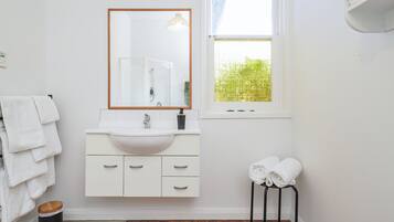 A bathroom with a white sink, mirror, and wooden floor. There are towels on a rack and a stool with towels.