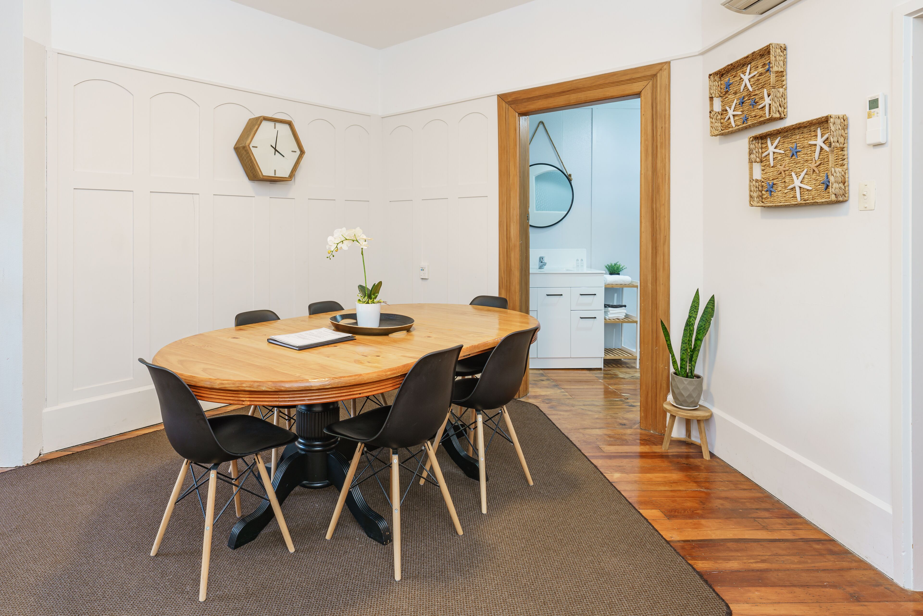 A dining area with a wooden table, black chairs, a clock, and decorative wall art.