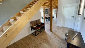 A wooden staircase leading to an upper level, a dining area with a table and chairs, and a door in the background. - Beach house "Sonne" (Lubmin)