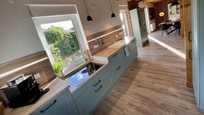 A modern kitchen with wooden beams, a large window, and a built-in stove. - Beach house "Sonne" (Lubmin)