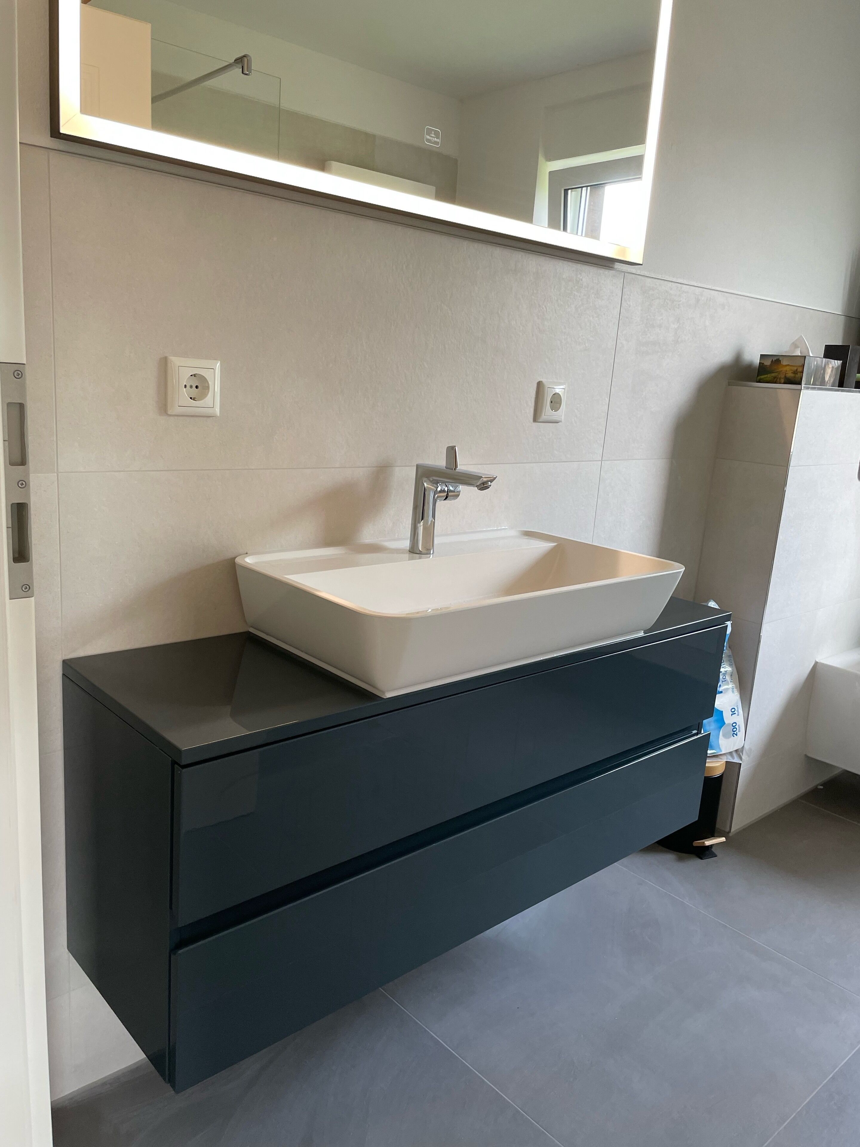 Un bagno moderno con un grande specchio, un lavandino bianco e un mobile contenitore scuro.