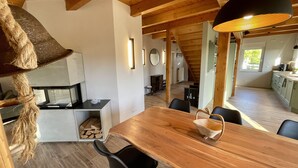 A modern kitchen with a wooden table and chairs, a hanging light fixture, and a view of the living area. - Beach house "Sonne" (Lubmin)