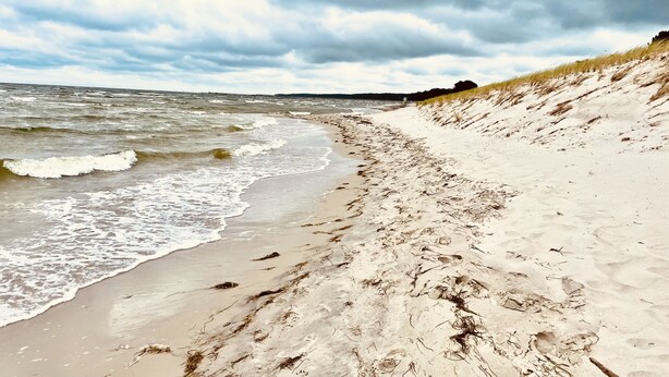 A sandy beach with waves, a grassy dune, and a cloudy sky. - Beach house "Sonne" (Lubmin)