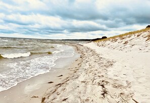 Une plage de sable avec des vagues, une dune herbeuse et un ciel nuageux.