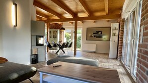 A modern living room with a wooden ceiling, a dining area with a brick wall, and a kitchen with a white countertop. - Beach house "Sonne" (Lubmin)