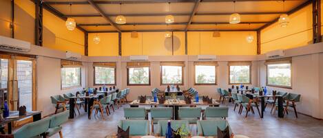 A spacious dining area with multiple tables and chairs, large windows, and hanging pendant lights.