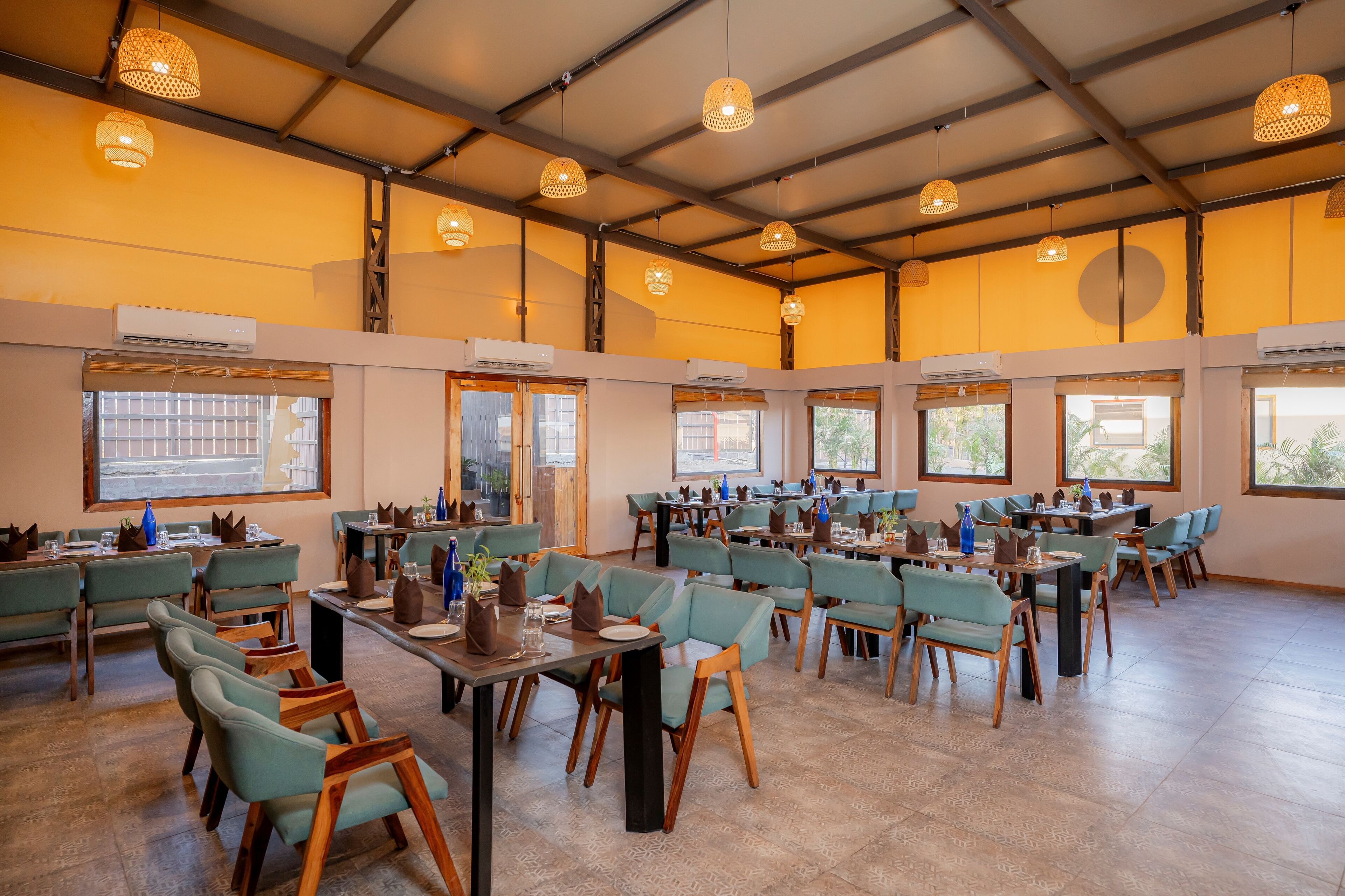 A spacious dining area with multiple tables and chairs, large windows, and hanging pendant lights.