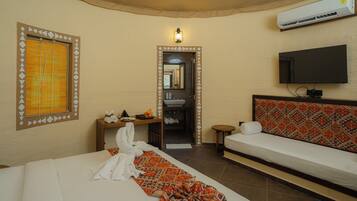 A hotel room with a bed, a sofa, a television, an air conditioning unit, and a bathroom visible through an open door.