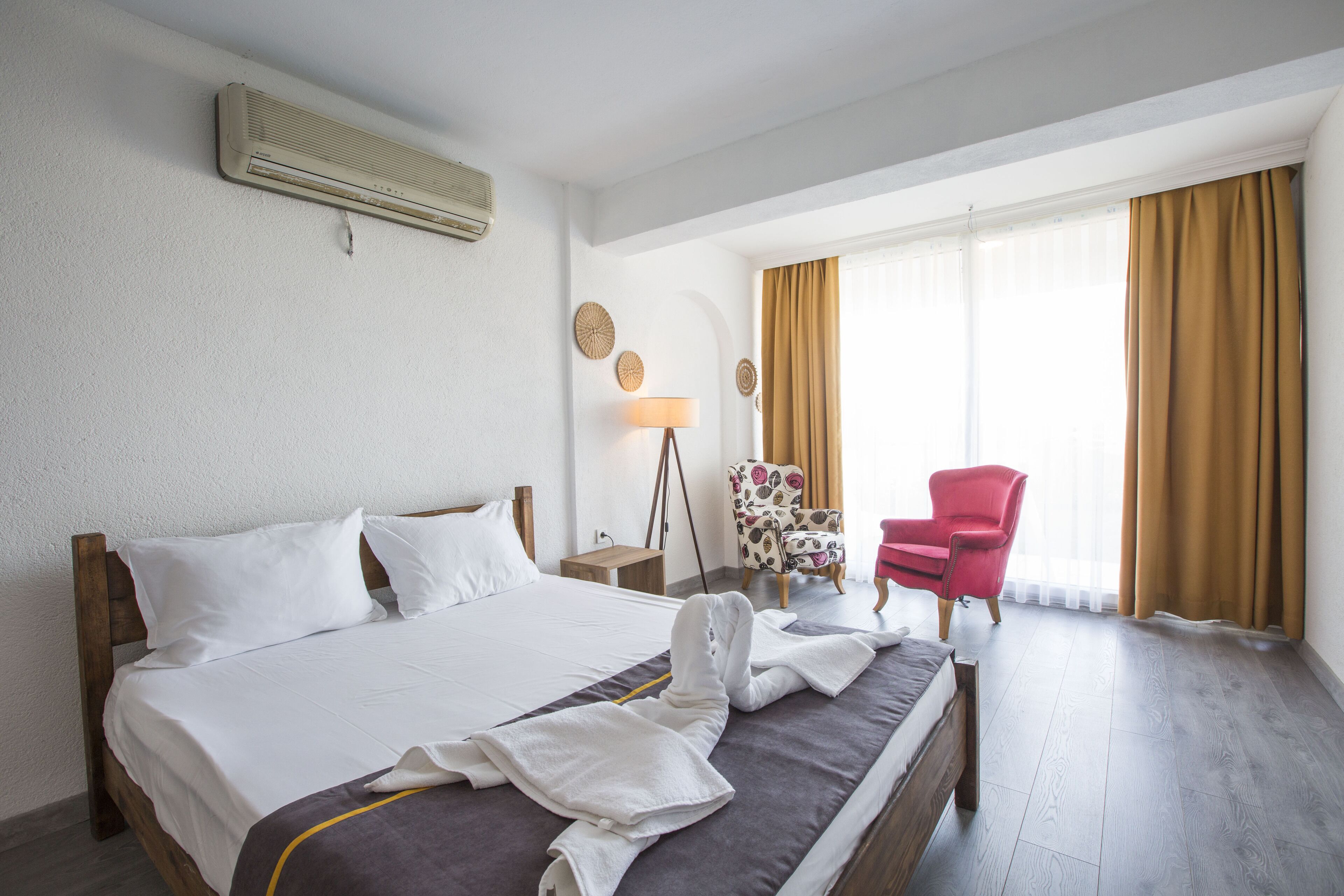 A hotel room with a bed, a chair, a lamp, and a window with curtains.