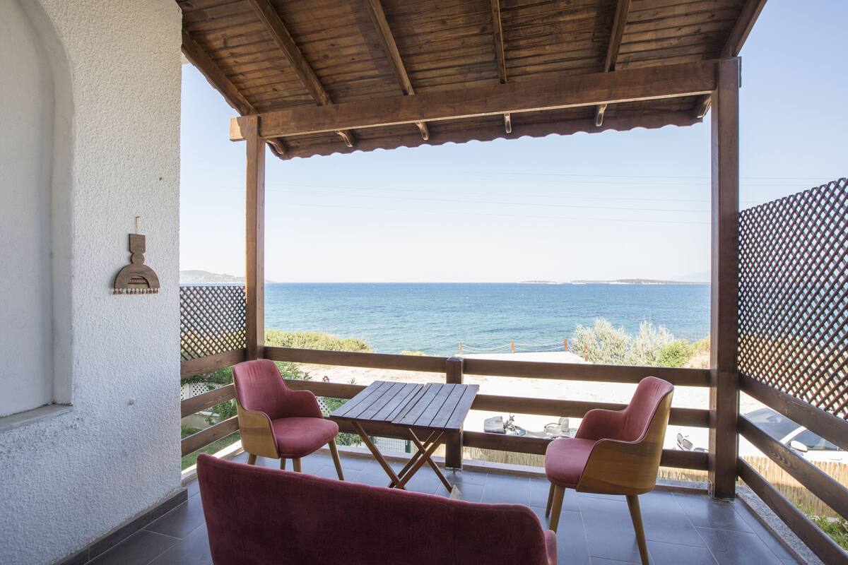 A covered outdoor seating area with a table and two chairs, overlooking a body of water and distant land.