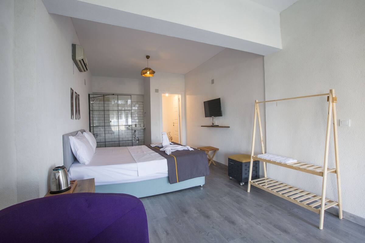 A modern hotel room with a bed, a TV, a wooden shelf, and a small table.